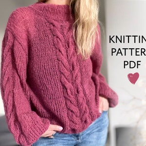 Op de afbeelding: Een roze gebreide trui met een kabelbreipatroon. De trui heeft een hoge hals en lange mouwen. De tekst "KNITTING PATTERN PDF" is zichtbaar in de afbeelding.