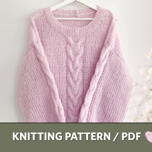 Op de afbeelding: Een lichtroze gebreide trui met een kabelpatroon in het midden en op de mouwen. De trui hangt aan een witte hanger. De tekst "KNITTING PATTERN / PDF" staat onderaan de afbeelding.