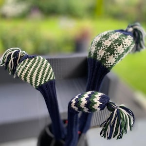 May include: Three golf club head covers in navy blue, green, and white. The covers have knitted patterns and tassels. The covers are designed to protect golf clubs. The covers are made of a knitted material.