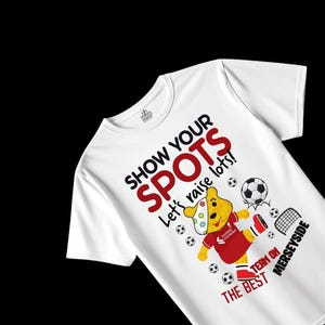 May include: White t-shirt featuring a cartoon bear kicking a football. The text "SHOW YOUR SPOTS" is in black and red, with "Let's raise lots!" below. The bear wears a red football kit with the text "TEAM ON MERSEYSIDE".
