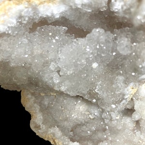 May include: A large, white geode with a rough, brown exterior. The geode is open, revealing a cavity filled with sparkling, white crystals.