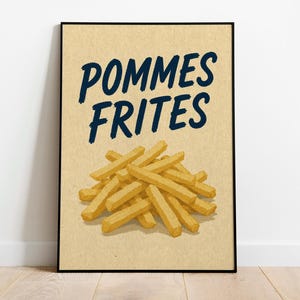 May include: A rectangular framed wall art print featuring a tan background with a pile of golden-yellow french fries illustrated in the center. Above the fries, the text POMMES FRITES is printed in a bold, dark blue, hand-lettered style font.