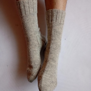 May include: A pair of light gray knitted socks. The socks are made of a textured yarn and have ribbed cuffs. The socks are shown from the ankles down, with the feet inside.