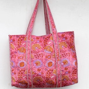Könnte beinhalten: Rosa Tragetasche mit floralem Muster. Die Tasche hat ein sich wiederholendes Design aus orangefarbenen und lila Blumen und Blättern auf rosa Hintergrund. Die Griffe und Kanten sind mit einem weiß-roten Streifenmuster versehen.