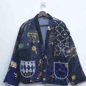 Könnte beinhalten: Eine Patchwork-Jacke in Marine-, Blau- und Goldtönen mit aufwendigen Stickmustern und zwei Vordertaschen. Die Jacke hängt an einem Holzbügel vor weißem Hintergrund. Das Design der Jacke umfasst florale und geometrische Motive.
