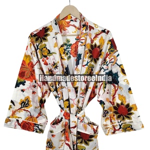 Könnte beinhalten: Weißer Bademantel mit floralem Druck, Bindverschluss und Taschen. Der Bademantel hat ein lebendiges Muster aus orangefarbenen, gelben und roten Blumen mit grünen Blättern. Der Text "Handmadestoreelndia" ist auf den Bademantel gedruckt.