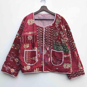 May include: A burgundy quilted jacket with a patchwork design. The jacket features embroidered floral patterns, two front pockets, and a striped lining. The sleeves are short, and the jacket is hanging on a wooden hanger against a white background.