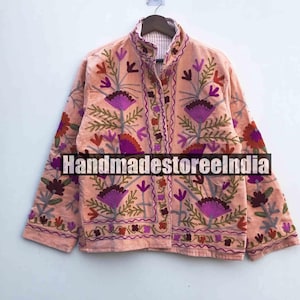 Könnte beinhalten: Pfirsichfarbene Jacke mit aufwendiger Blumenstickerei in Lila, Grün und Rot. Die Jacke hat einen hohen Kragen und eine Knopfleiste. Der Text "Handmadestoreindia" ist auf der Vorderseite aufgedruckt.