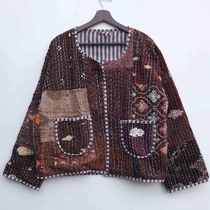 May include: A brown patchwork jacket with a round collar and two front pockets. The jacket features various fabric patterns and decorative stitching. The lining is striped. The jacket is hanging on a wooden hanger against a white background.