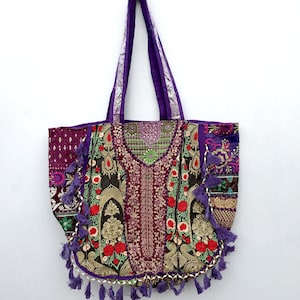 May include: A large, decorative tote bag with a purple handle and intricate embroidery. The bag features a patchwork design with red, gold, and black floral patterns, accented with purple tassels and gold trim. The bag is hanging against a white background.