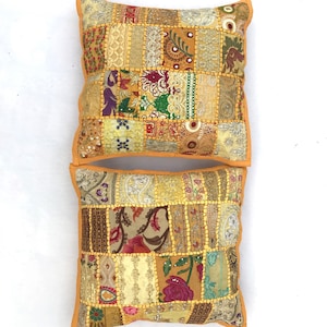 Puede incluir: Dos cojines decorativos con un diseño de patchwork. Los cojines están hechos de varias telas en tonos de amarillo, marrón y beige. La tela está adornada con bordados y lentejuelas. Los cojines tienen un borde amarillo sólido.