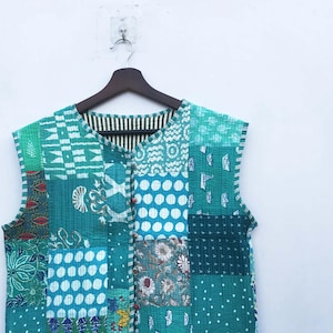 May include: A teal blue quilted vest with a patchwork design. The vest has a button closure and a white trim around the edges.