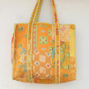 Könnte beinhalten: Eine große gelbe Patchwork-Tragetasche mit gestepptem Design und gelben und weißen Streifen an den Griffen.