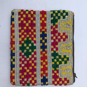 Könnte beinhalten: Eine farbenfrohe, rechteckige Textiltasche mit Reißverschluss. Das Design zeigt ein kariertes Muster in Rot, Gelb, Grün und Blau, akzentuiert mit silbernen Zierleisten und Pailletten. Die Kanten sind mit einem braunen Rand versehen.