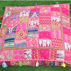 Könnte beinhalten: Ein quadratisches Patchwork-Kissen in Rosatönen mit verschiedenen gestickten Mustern. Das Kissen hat einen Rand aus Quasten in verschiedenen Farben. Das Patchwork-Design umfasst florale und geometrische Motive.