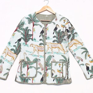 Könnte beinhalten: Eine weiße gesteppte Jacke mit einem grünen, braunen und gelben Dschungelprint mit Tukanen, Leoparden und Palmen. Die Jacke hat einen Knopfverschluss und zwei aufgesetzte Taschen.