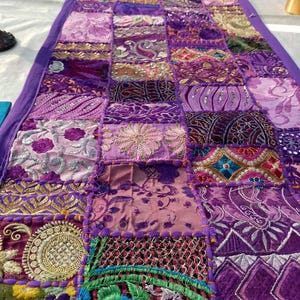 Peut inclure: Chemin de table patchwork violet, compos&eacute; de divers tissus et textures. Le chemin de table rectangulaire a une bordure violette unie et est orn&eacute; de motifs floraux et g&eacute;om&eacute;triques brod&eacute;s. Mesure environ 150 cm de long.
