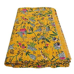 Könnte beinhalten: Gefaltete gelbe Steppdecke mit einem Blumenmuster mit rosa, weißen und grünen Blumen und weißen Vögeln. Die Steppdecke ist mit weißem Faden genäht und die Kanten sind mit einem gelben Rand versehen.