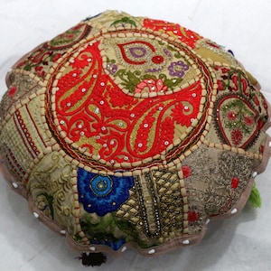 Könnte beinhalten: Ein rundes, mehrfarbiges, besticktes Bodenkissen mit beigefarbenem Hintergrund. Das Kissen besteht aus Patchwork-Stoff mit verschiedenen Blumen- und Paisley-Mustern. Das Kissen ist mit Perlen und Pailletten verziert.