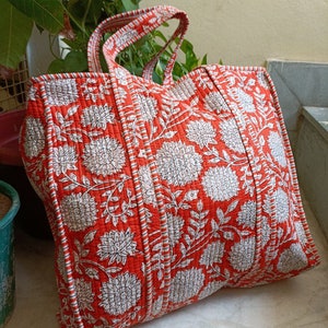 Könnte beinhalten: Eine große, rote Tragetasche mit einem weißen Blumenmuster. Die Tasche hat zwei Henkel und ist aus gestepptem Stoff.