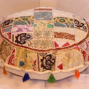 Könnte beinhalten: Runder Bodenkissen mit Patchwork-Design. Das Kissen hat eine Vielzahl von Stoffmustern in Beige, Creme und anderen Farben. Es hat eine dekorative Bordüre und bunte Quasten um den Sockel.