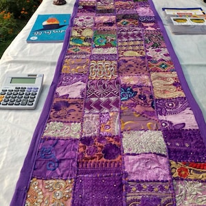Peut inclure: Chemin de table patchwork rectangulaire dans diverses nuances de violet. Le chemin de table a une bordure violette unie et est fait de divers tissus &agrave; motifs. Le design comprend des &eacute;l&eacute;ments brod&eacute;s et textur&eacute;s, cr&eacute;ant une pi&egrave;ce d&eacute;corative.