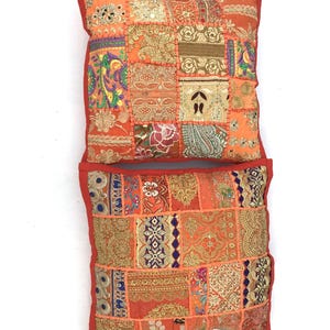 May include: Two orange patchwork throw pillows with gold embroidery and colorful accents. The pillows are made of a variety of fabrics and have a bohemian style.