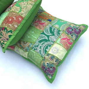 Op de afbeelding: Twee groene patchwork kussens met kleurrijke borduursels en pailletten. De kussens zijn gemaakt van verschillende stoffen en texturen, waardoor een unieke en bohemian look ontstaat.