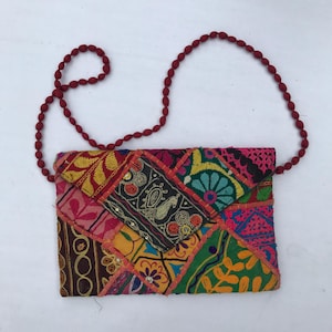 Könnte beinhalten: Eine bunte Patchwork-Umhängetasche mit einem roten Perlenriemen. Die Tasche besteht aus quadratischen, bestickten Stoffen in Rot-, Rosa-, Gelb-, Grün- und Blautönen. Die Tasche hat eine rechteckige Form.