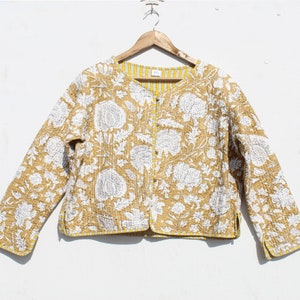 Könnte beinhalten: Eine gesteppte Jacke mit gelbem und weißem Blumendruck und Knopfleiste. Die Jacke hat lange Ärmel und eine verkürzte Länge.
