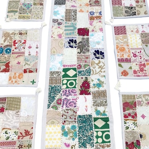 Könnte beinhalten: Ein Set aus Patchwork-Tischläufern und Platzsets in verschiedenen Farben und Mustern, darunter florale, geometrische und Paisley-Designs. Der Stoff ist eine Mischung aus Baumwolle und Seide, und die Kanten sind mit einem weißen Besatz versehen.