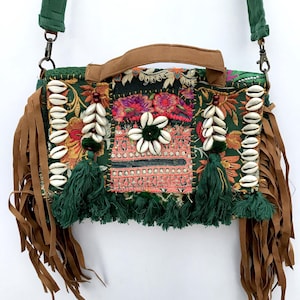 Könnte beinhalten: Grüne und braune Umhängetasche mit Patchwork-Design. Die Tasche hat Blumenstickereien, Kaurischalen und braune Fransen. Sie hat einen braunen Griff und einen verstellbaren grünen Riemen.