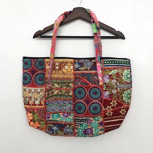 Könnte beinhalten: Eine Patchwork-Tragetasche mit einer Vielzahl von bunten, bestickten Stoffquadraten. Die Tasche hat einen schwarzen Reißverschluss und passende Stoffgriffe. Die Griffe sind eine Mischung aus rosa, roten und grünen Blumenmustern.