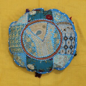 Peut inclure: Un coussin rond en patchwork bleu et or avec des broderies complexes et une bordure perlée.