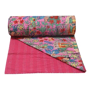 Puede incluir: Una colcha enrollada, rosa, con estampado floral y un reverso rosa liso en contraste. La parte superior presenta un diseño vibrante con flores, figuras y follaje en varios colores. La colcha está hecha de una tela suave y acolchada.