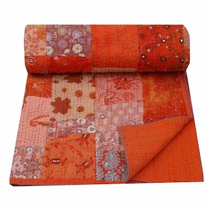 Könnte beinhalten: Eine orangefarbene Patchwork-Steppdecke mit verschiedenen Blumen- und Paisley-Mustern. Die Steppdecke besteht aus mehreren Stoffquadraten in Orange-, Rot- und Rosatönen, mit aufwendigen Nähten und einem gerollten Rand. Die Steppdecke ist gefaltet.