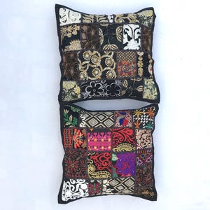 May include: Two decorative throw pillows with a patchwork design. The pillows are made of different fabrics and colours, including black, white, red, green, and gold. The pillows have a black border.