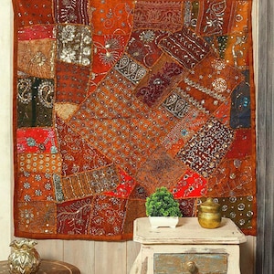 May include: A large, patchwork textile wall hanging in shades of orange, red, and brown. The design incorporates various patterns and textures, with metallic accents. The textile is rectangular and appears to be mounted on a wall.