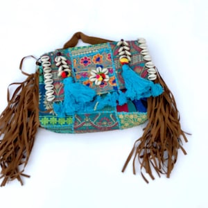 Könnte beinhalten: Eine bunte Patchwork-Umhängetasche mit braunen Fransen und einem braunen Griff. Die Tasche hat blaue Quasten, Muschelakzente und Blumenstickereien. Die Tasche ist im Bohème-Stil.