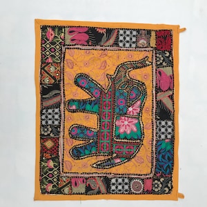 Könnte beinhalten: Quadratischer Textilartikel mit Elefantenmuster. Der Elefant ist hauptsächlich türkis, rosa und grün, vor einem gelben Hintergrund. Der Rand ist ein Patchwork aus verschiedenen Mustern und Farben, mit einem orangefarbenen Rand.