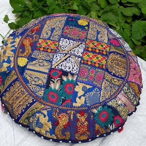May include: Round, patchwork floor cushion in shades of blue, gold, pink, and red. The cushion features intricate embroidered patterns and a beaded edge. This decorative cushion is perfect for adding a touch of bohemian flair to any room.