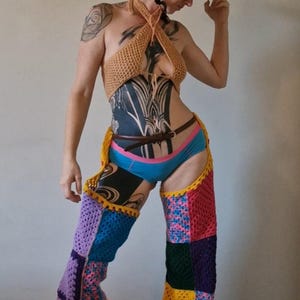 May include: A vibrant crochet ensemble comprising a halter top, chaps, and a cowboy hat. The chaps and hat are patchwork, with squares of diverse colours. The halter top is tan, and the chaps are a mix of blue, yellow, pink, and purple.