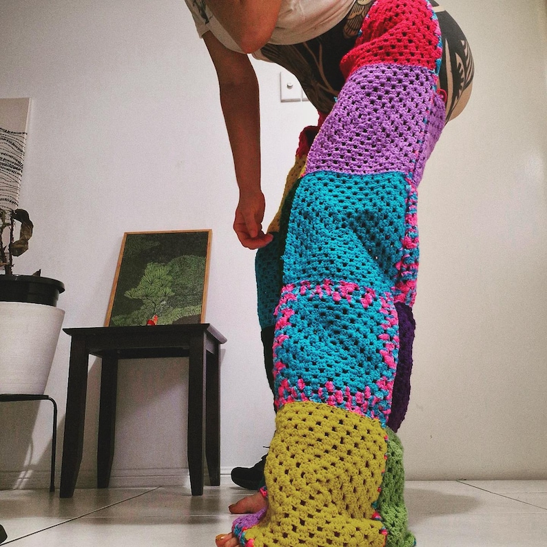 May include: A pair of colourful, patchwork crochet trousers. The trousers feature large squares of various colours, including red, purple, teal, yellow, and green, with pink accents. The open weave design is visible.