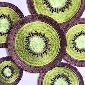 Può includere: Cinque toppe ricamate a forma di kiwi con frange marroni. Le toppe a forma di kiwi sono verdi con semi neri e un centro verde chiaro.