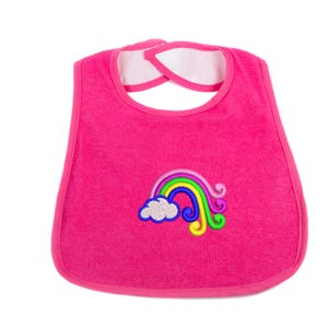 Op de afbeelding: Een felroze baby slabbetje met een geborduurd regenboog- en wolkenontwerp. Het slabbetje heeft een afgeronde vorm met een witte voering rond de nek en een roze rand. De regenboog heeft gele, groene, blauwe en paarse kleuren.