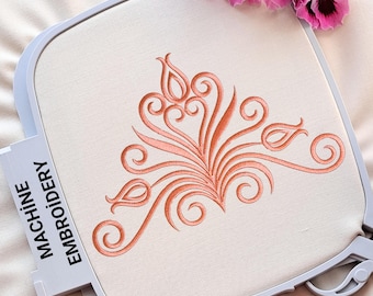 May include: A close-up of a white embroidery hoop with a pink floral design embroidered on the fabric. The design features a stylized floral motif with delicate swirls and leaves.