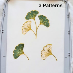 May include: White fabric featuring three embroidered ginkgo leaf patterns in green and gold. The text "3 Patterns" is at the top. The leaves are intricately stitched, arranged in a decorative design, highlighting the embroidery.