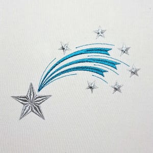May include: Embroidered design of a shooting star with silver stars and a teal blue trail on a white background. The design features a large star at the beginning of the trail and several smaller stars scattered along the arc.