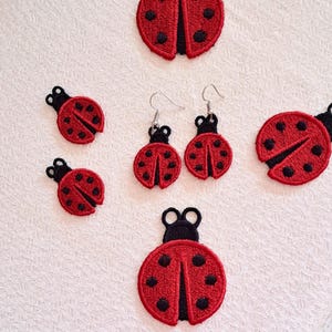 May include: A set of six red and black ladybug earrings and charms. The earrings are dangling and the charms are flat. The ladybugs are embroidered with black details.