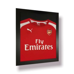 May include: A red football shirt with white accents and the Puma logo. The shirt has the text "Fly Emirates" and the Arsenal logo on the front.